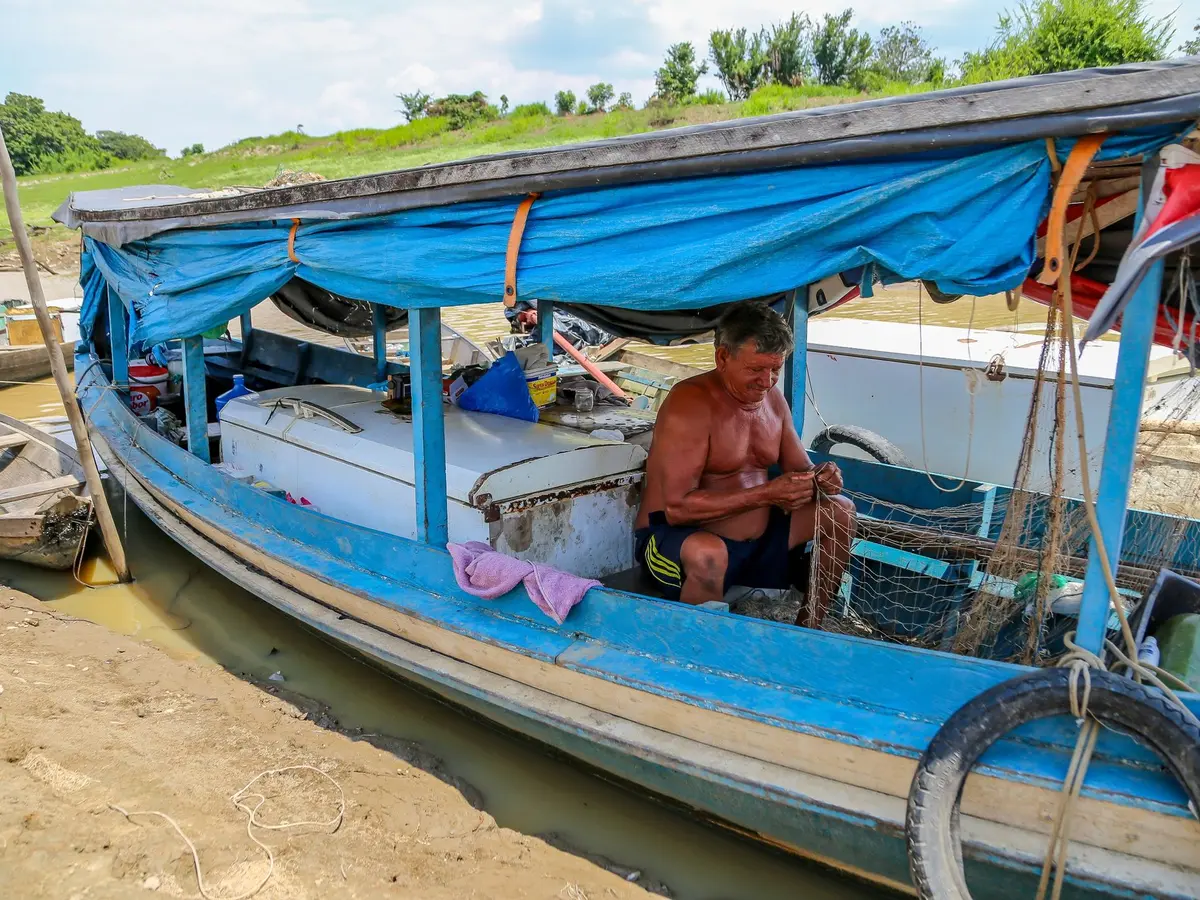 A fisherman sits in his boat, almost dry, mending a net. The drought is not only causing difficulties for the river dwellers when it comes to fishing, but also for transportation. Villages in the region are linked by rivers.