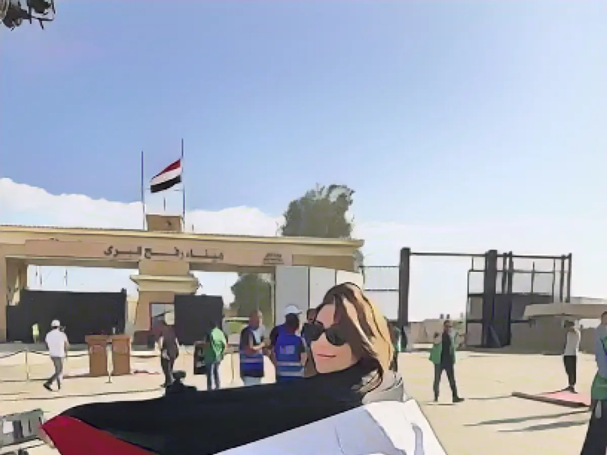 Эль-Хельбави стоит на пограничном переходе Рафах между Газой и Египтом с палестинским флагом, перекинутым через спину.