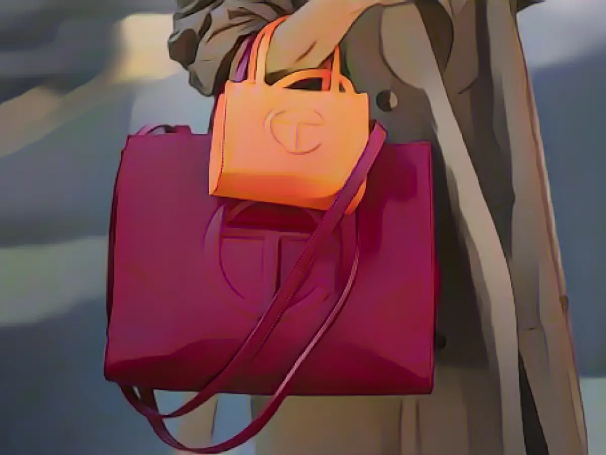 Samia Laaboudi poartă un trenci bej, o geantă portocalie neon de la Telfar și o geantă burgundă de la Telfar, în timpul Săptămânii Modei de la New York, pe 14 septembrie 2022, în New York.
