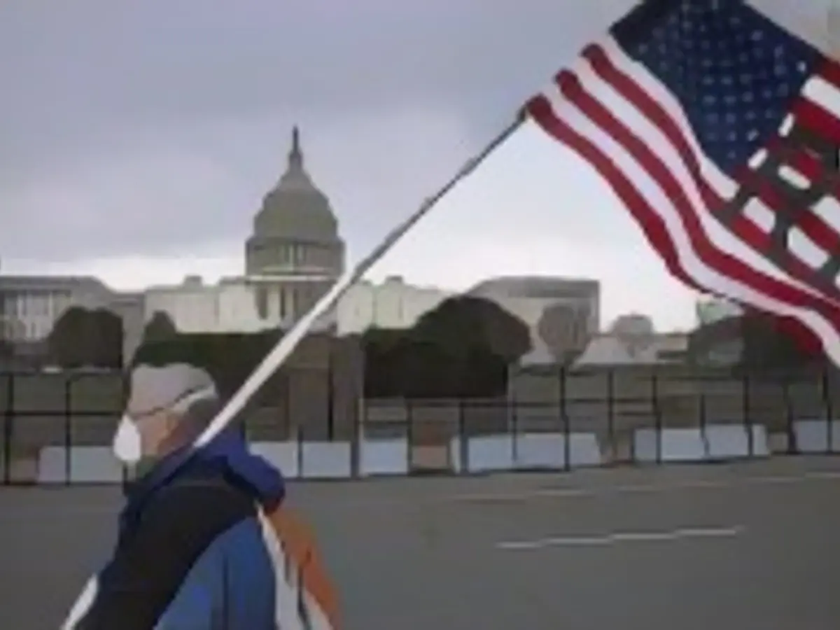 WASHINGTON, DC – 8. JANUAR: Ein Demonstrant geht vorbei, während die amerikanische Flagge auf Halbmast weht. 8. Januar 2021 im Capitol in Washington, DC. Die Sprecherin des Repräsentantenhauses, Nancy Pelosi, ordnete das Hissen von Flaggen am Gebäude mit halbem Personal an, um den Polizeibeamten des Kapitols, Brian Sicknick, 42, zu ehren, der am 6. Januar im Kapitol mit Pro-Trump-Randalierern kämpfte. Er starb, nachdem er während eines Konflikts verletzt worden war. Ein Veteran mit 12 Dienstjahren. (Foto von John Moore/Getty Images)