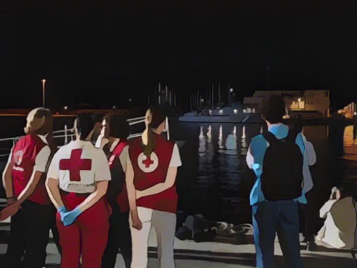Члены Красного Креста ждут у ангара в Каламате (Греция), где временно разместили мигрантов после потопления рыболовецкого судна с сотнями пассажиров.