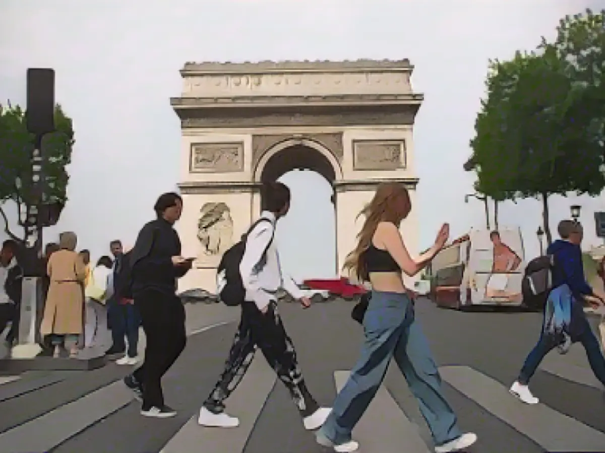 Fußgänger überqueren am 29. April 2022 in Paris die Champs Elysées vor dem Arc de Triomphe-Denkmal. Frankreichs Covid-19-Risikostufe ist Stufe 3, also „hohes“ Risiko.