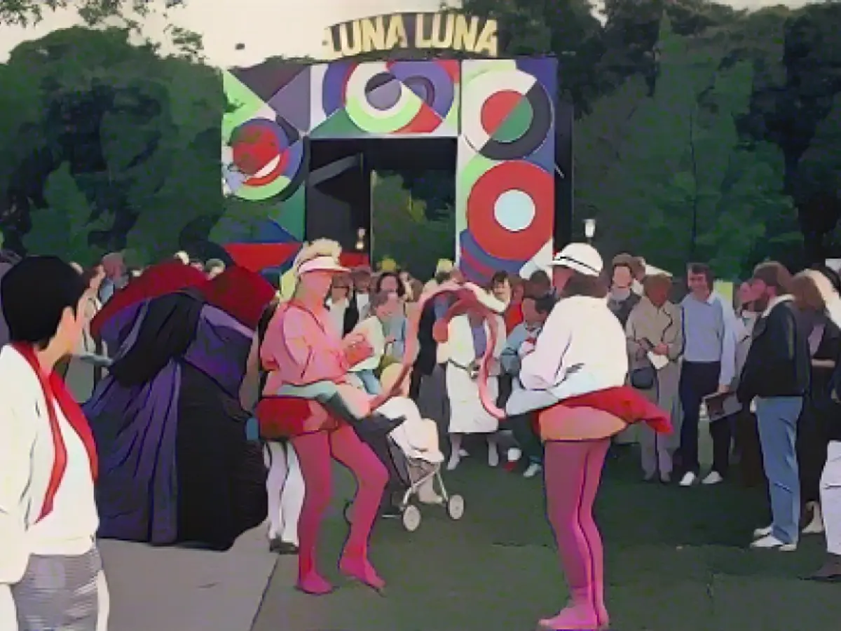 Артисты - естественно, в костюмах жокеев, катающихся на фламинго, - развлекают толпу перед аркой, созданной по проекту Сони Делоне, у входа в Luna Luna.