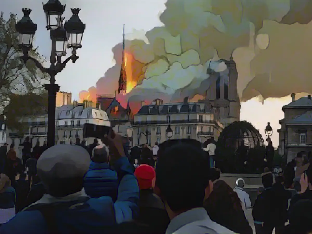 Oamenii privesc cum arde catedrala Notre-Dame, monument istoric, în centrul Parisului, la 15 aprilie 2019- Investigațiile nu au identificat cauza exactă a incendiului.