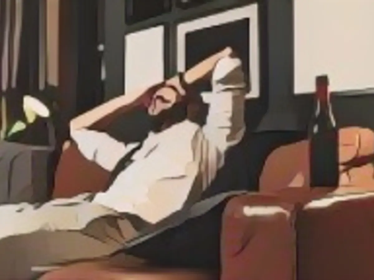 Vista laterale di un giovane uomo seduto sul divano del suo salotto, che si gode una birra dopo una lunga giornata di lavoro da casa