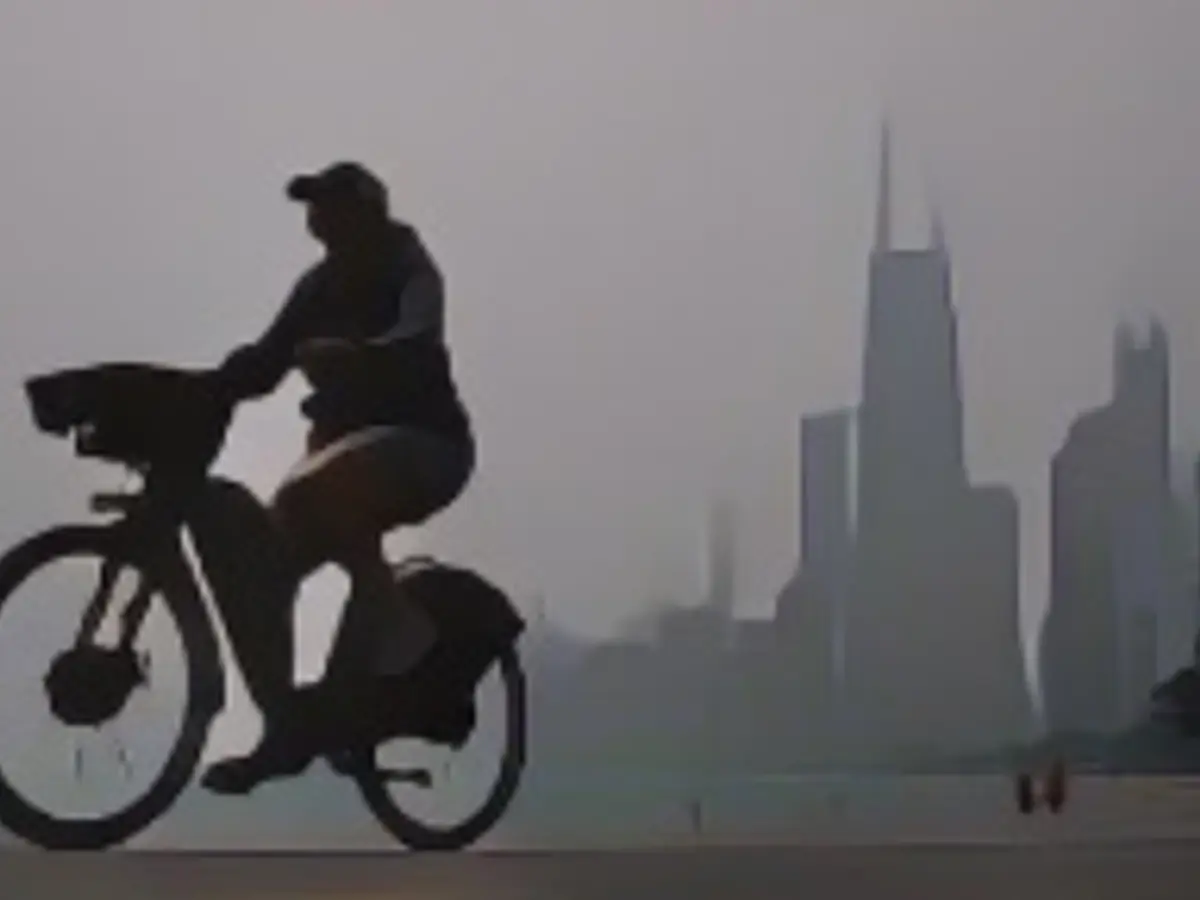 O persoană se plimbă pe bicicletă pe malul lacului Michigan, în timp ce centrul orașului Chicago este acoperit de ceața provocată de incendiile canadiene, marți, în Chicago.