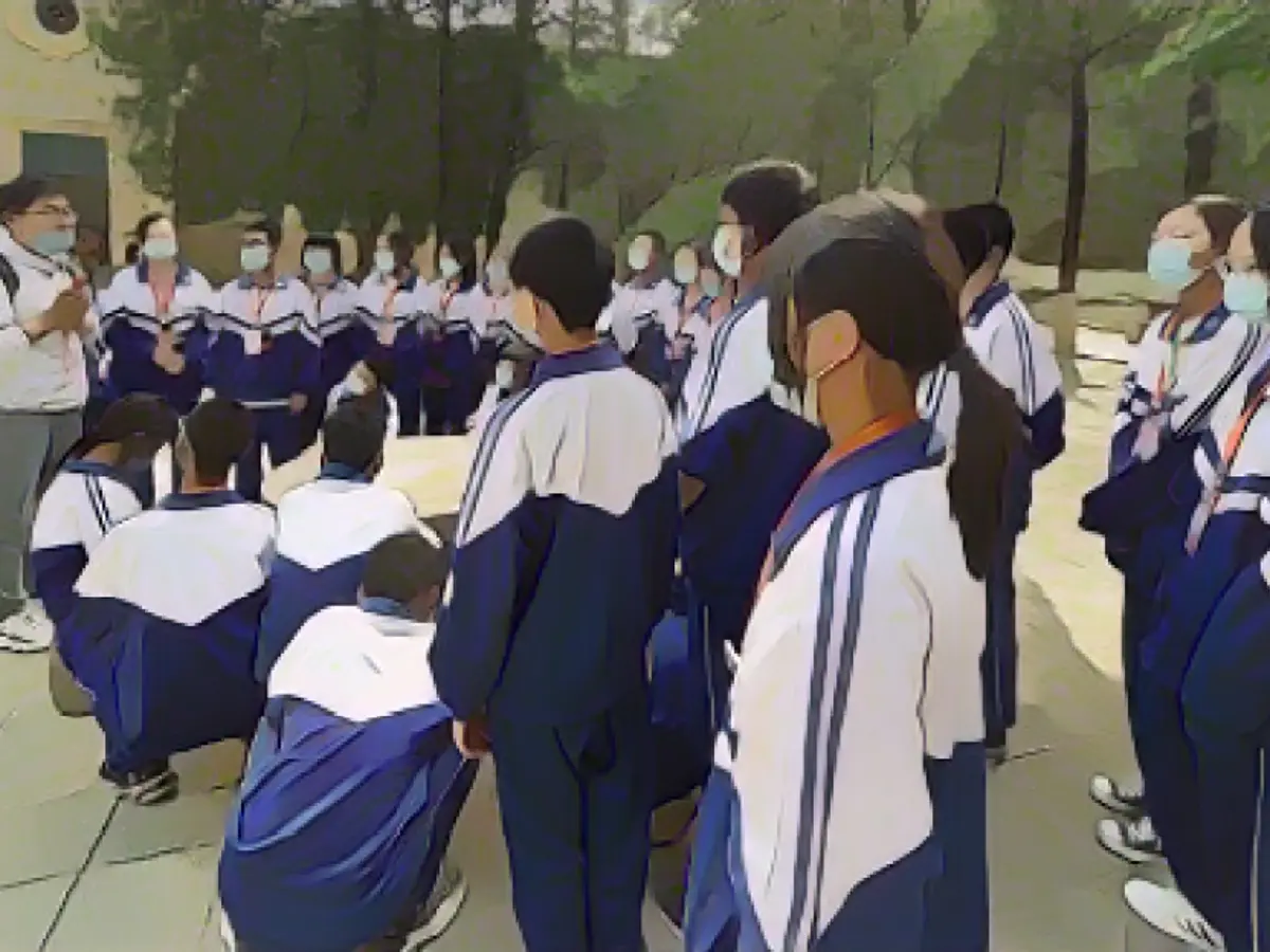 Ученики в школьной форме слушают лекцию о первых годах существования коммунистической партии под открытым небом перед историческим зданием в Яньане.