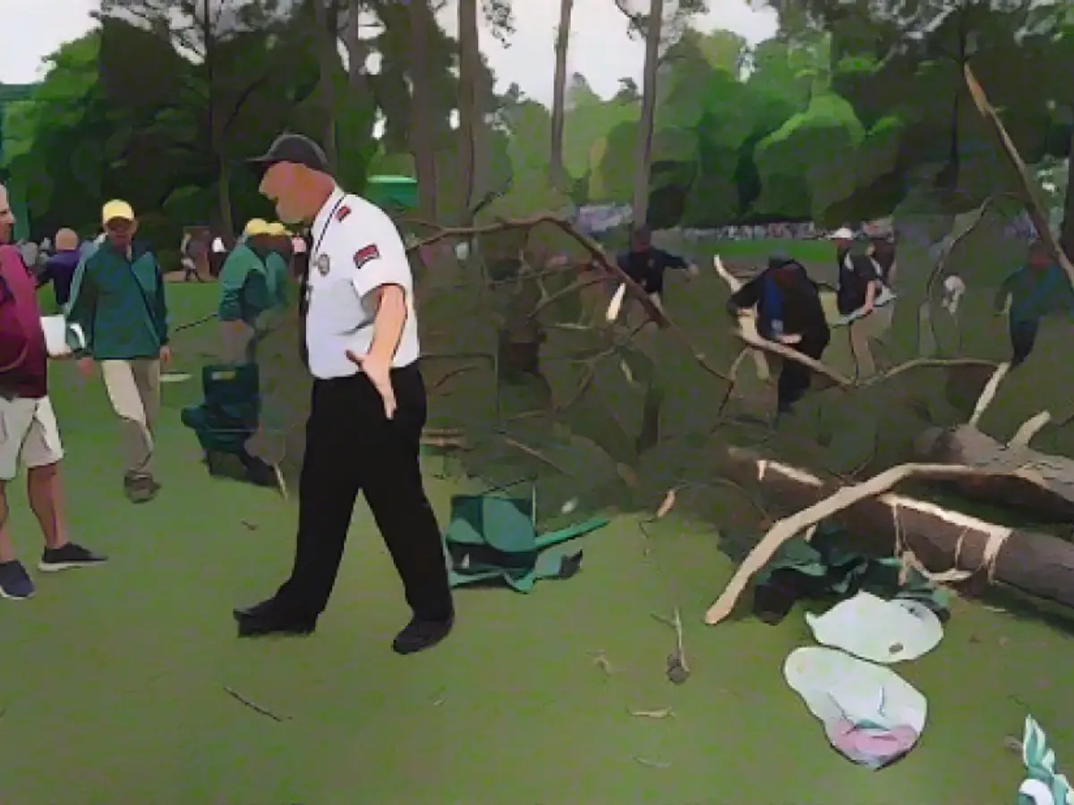 Un agent de securitate îndepărtează oamenii de copacii care au fost doborâți vineri pe gaura 17 a Augusta National Golf Club. Nu s-au înregistrat răniți.