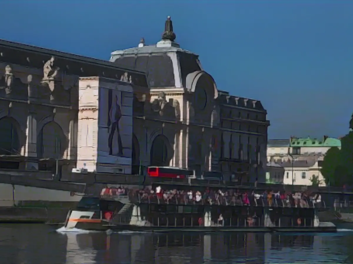Turistler 22 Ağustos 2023'te Seine Nehri üzerinde, arka planda Orsay Müzesi'nin yer aldığı açık bir gezi teknesiyle Paris'i geziyor.