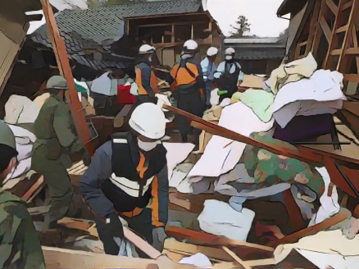 Des pompiers et des membres de la Force japonaise d'autodéfense sauvent un homme âgé d'une maison effondrée le 3 janvier 2024 à Suzu, Ishikawa, Japon.
