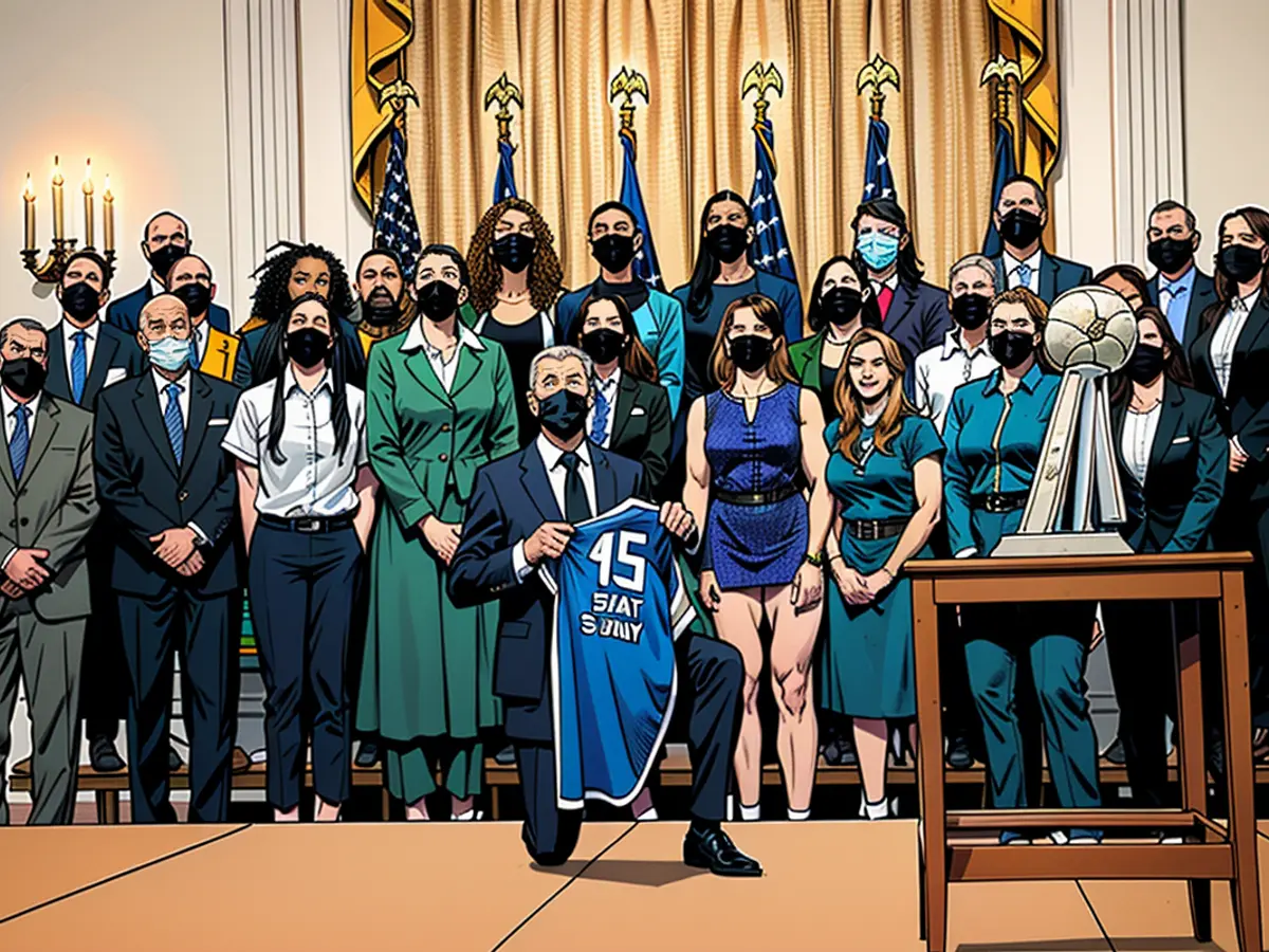 El presidente de Estados Unidos, Joe Biden, sostiene una camiseta que le regalaron mientras se arrodilla para una fotografía de grupo con miembros del equipo de baloncesto femenino Seattle Storm 2020 WNBA Championship en la Casa Blanca en Washington, Estados Unidos, 23 de agosto de 2021.